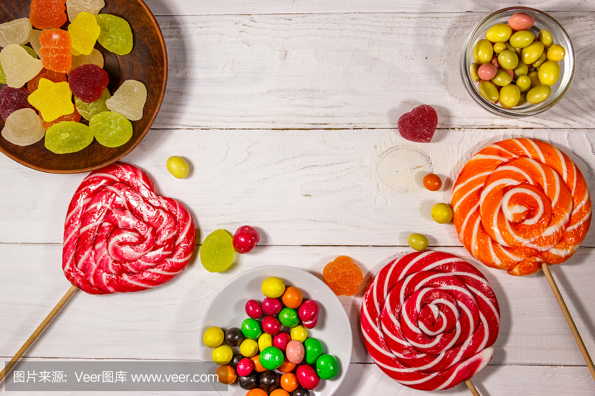 白色的木桌上放着五颜六色的巧克力糖果、棒棒糖和果冻糖果